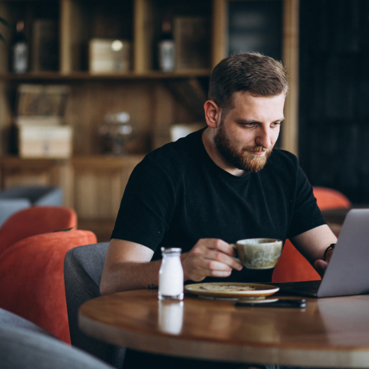 man drinks coffee and works in a cafe with a laptop